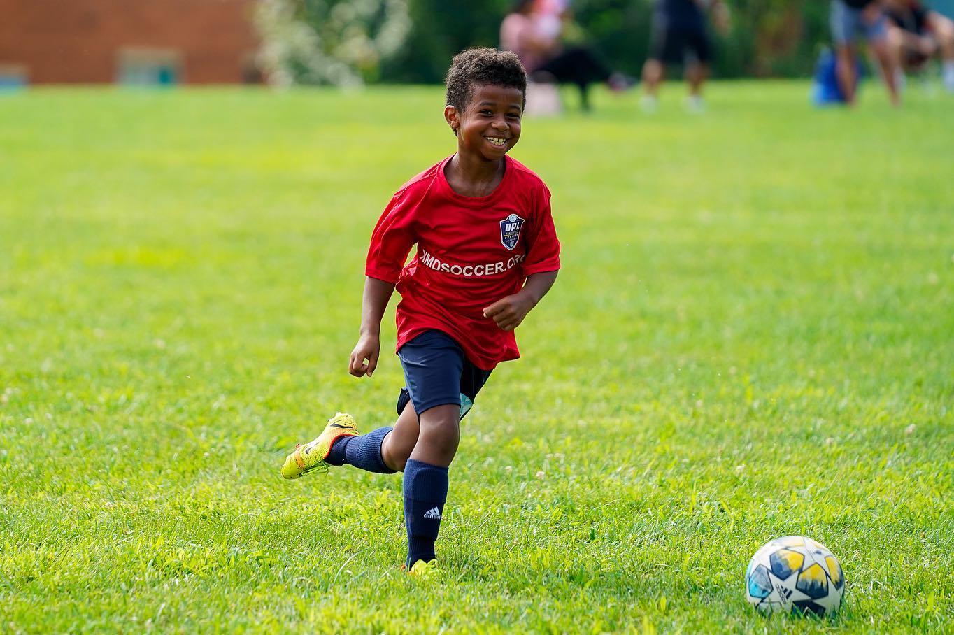 A young XMD Soccer Academy player smiling as he chases the ball